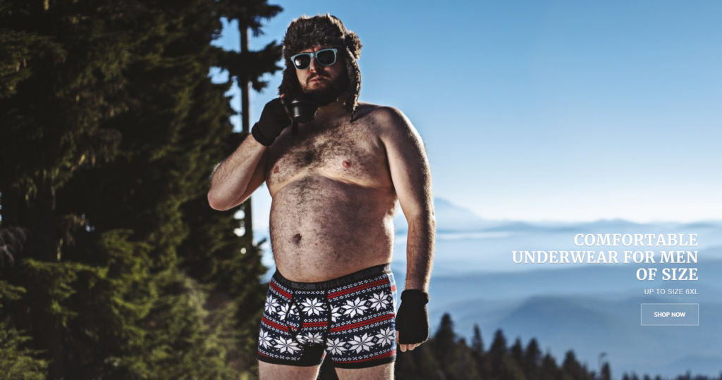 A smallfat white man is shown standing in boxers and winter gloves outside against a backdrop of mountains in the sun. He's wearing sunglasses and a furry hat, and holding a camping mug.