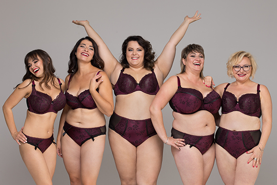 Five white women ranging in size from very thin to medium fat stand against a gray background. They're each wearing matching purple bra and panty sets and look relaxed and happy.