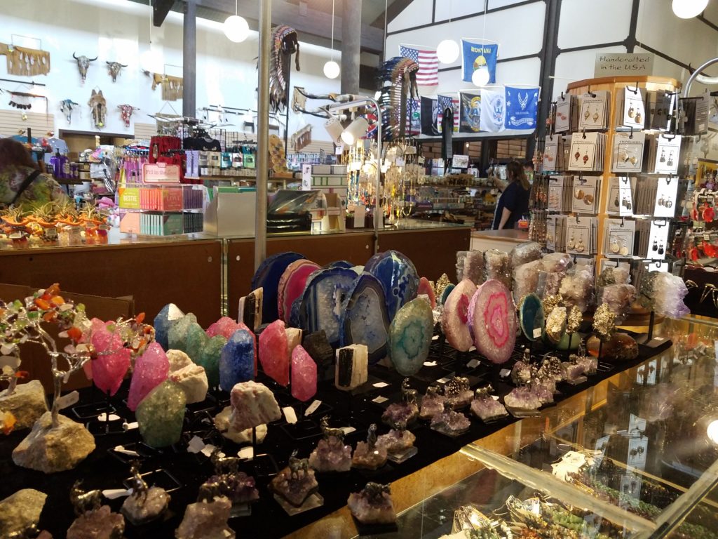 The gift shop at 50,000 Silver Dollar, which does indeed have fifty thousand silver dollar coins in its counters and on its walls. A cluttered set of counters, shelves and racks holds a variety of gemstones, figurines, cards, and jewelry.