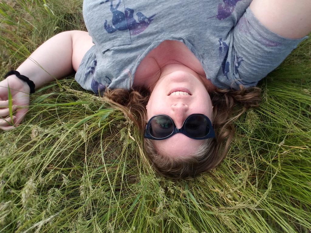 A fat white woman lies on her back in tall grass.