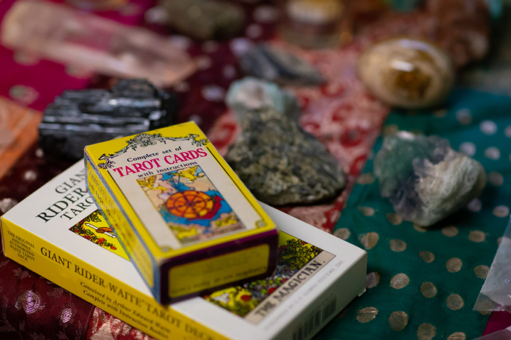 Two boxes of tarot cards and a number of crystals for crystal healing and energy work rest on a colorful fabric cloth in green, red and orange tones.