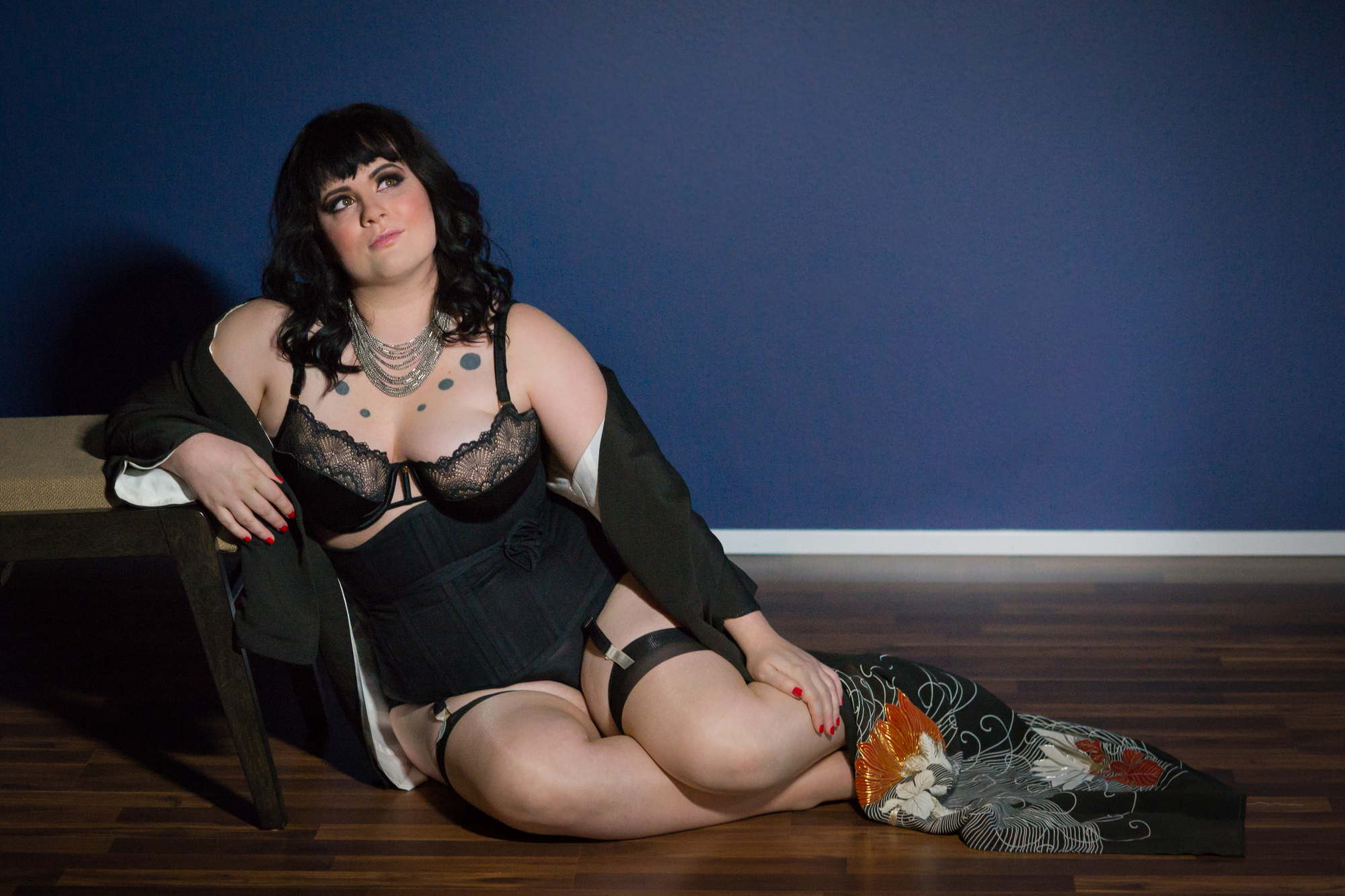 A woman in black lingerie leans against a bench on the floor during an LGBT friendly photo shoot in the PNW