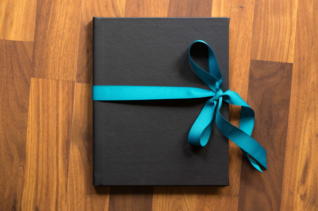 A gift box with a bright blue bow sits on a wooden floor during a small business photo session