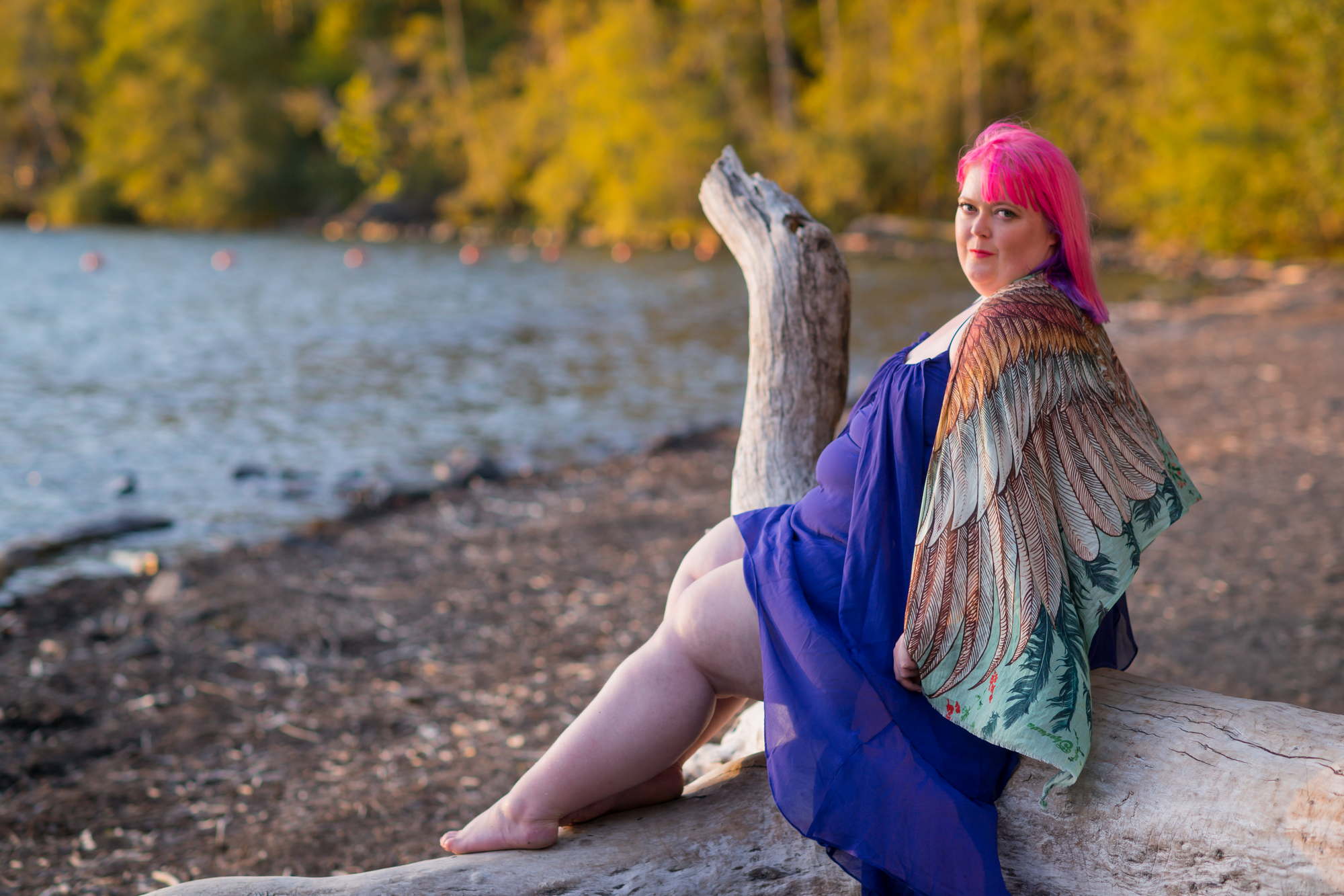 A fat woman with pink hair poses with a sultry look on driftwood on the beach in Seattle 