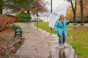 A woman holding an umbrella splashes in a puddle at a park in WA