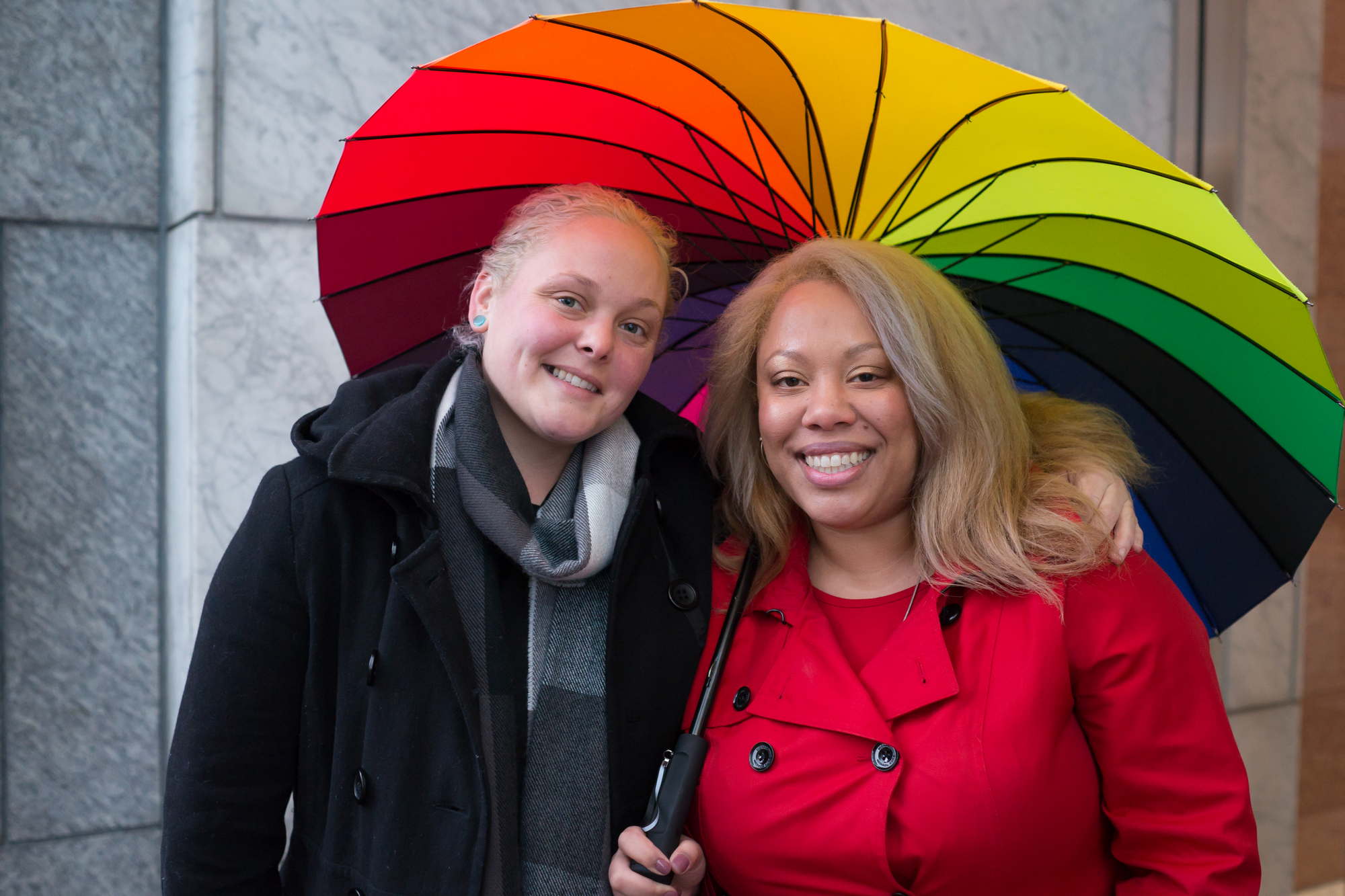 Two women pose together under a rainbow umbrella for an lgbt friendly photo shoot