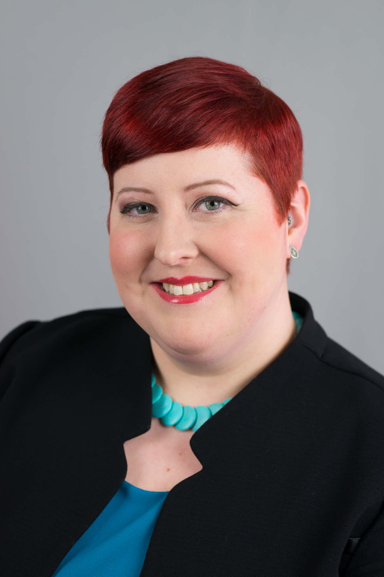 A fat woman with red hair and red lipstick smiles confidently at the camera for a business headshot