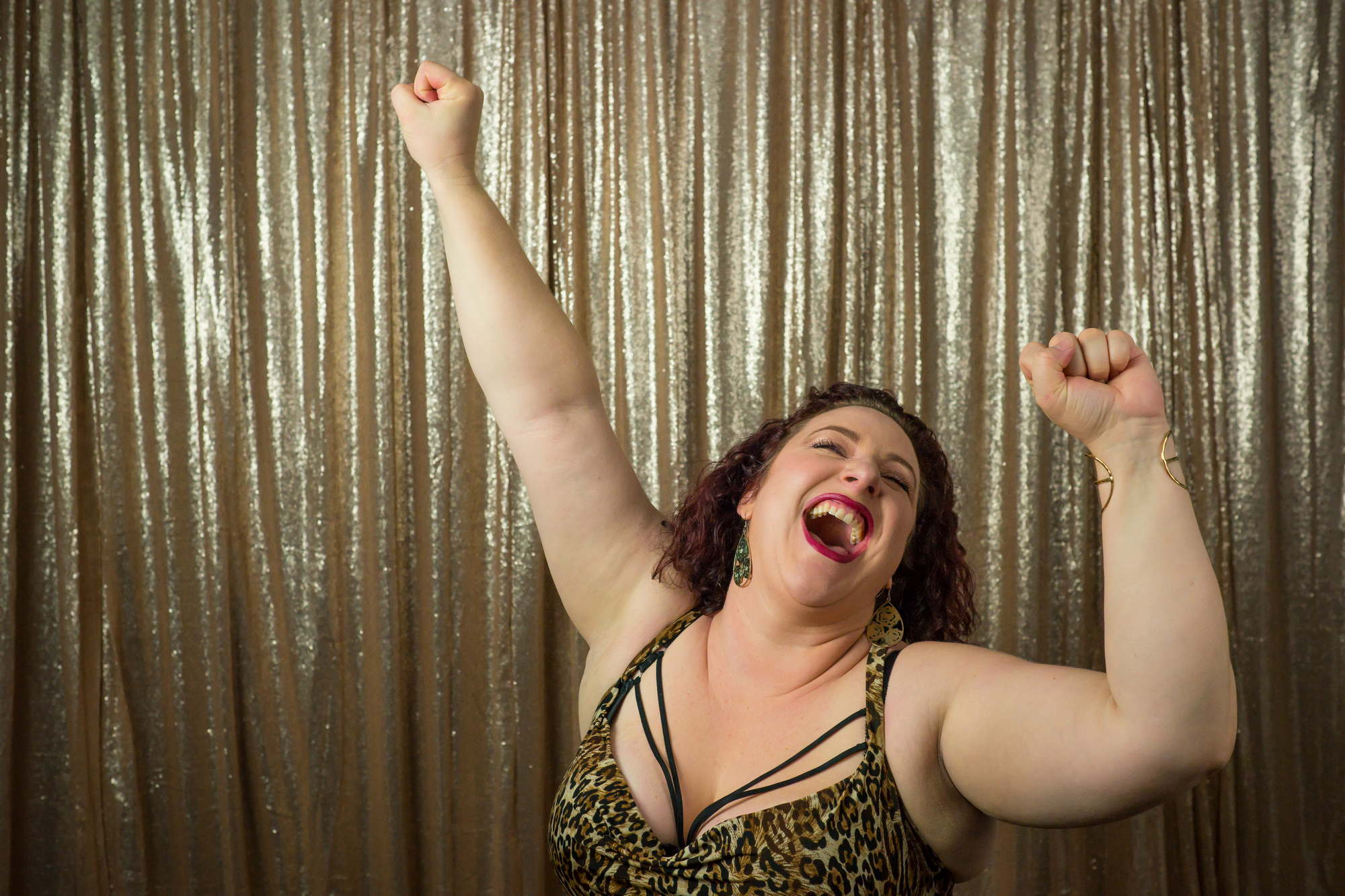 A fat woman dances joyfully in front of a gold curtain
