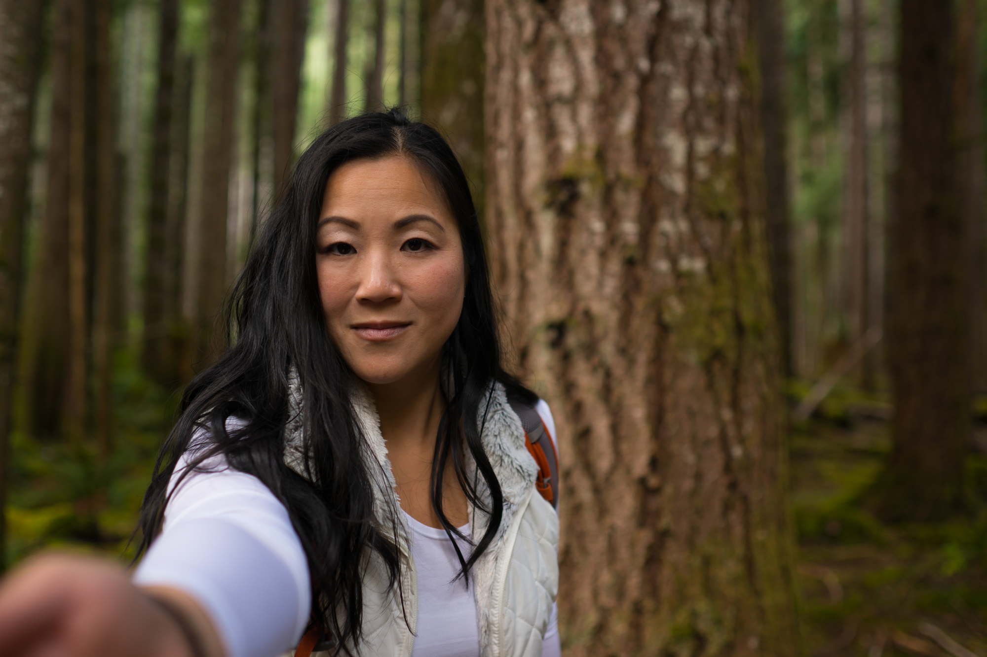 A woman with long dark hair reaches towards the camera during an outdoor portrait photo shoot