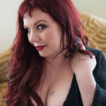 A woman with red hair looks playfully at the camera during a boudoir photo session
