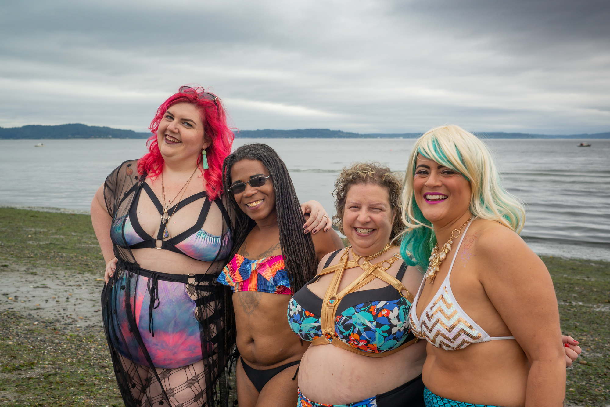 A group of women in swimsuits pose joyfully on a beach in Seattle