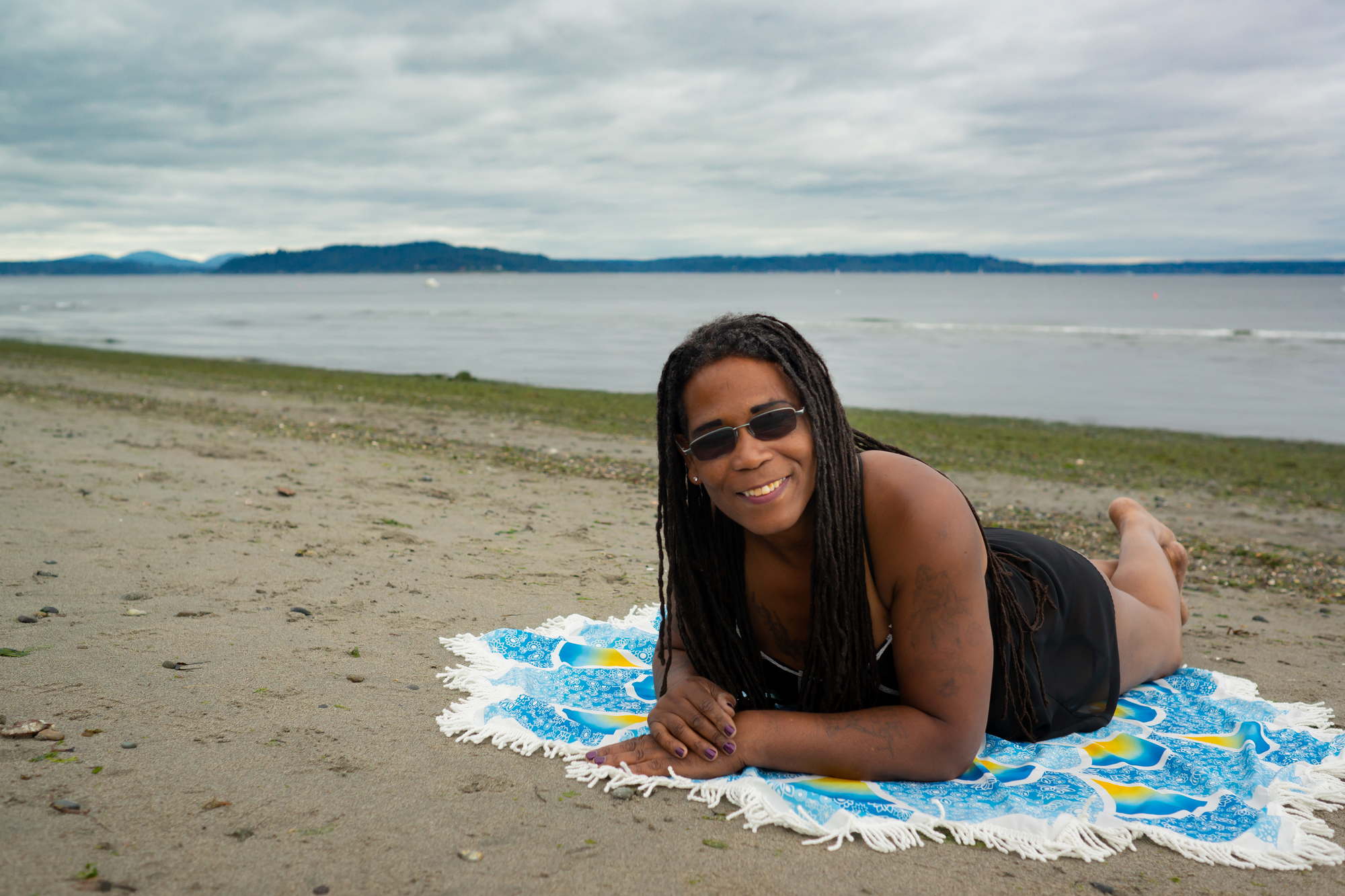 A Black woman lays looking joyful on a beach in Seattle for a fat friendly photo shoot