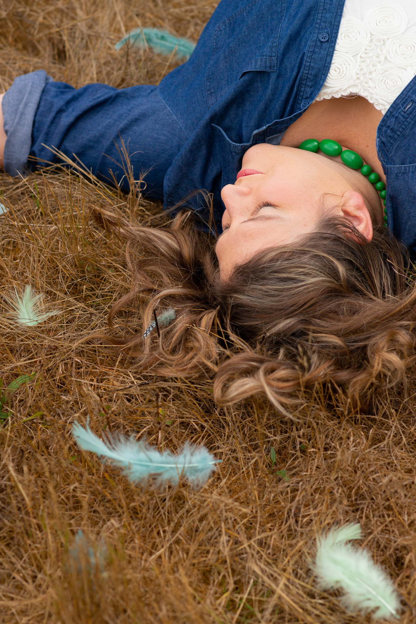 A woman wearing a green necklace lays on the grass for an outdoor portrait photo shoot