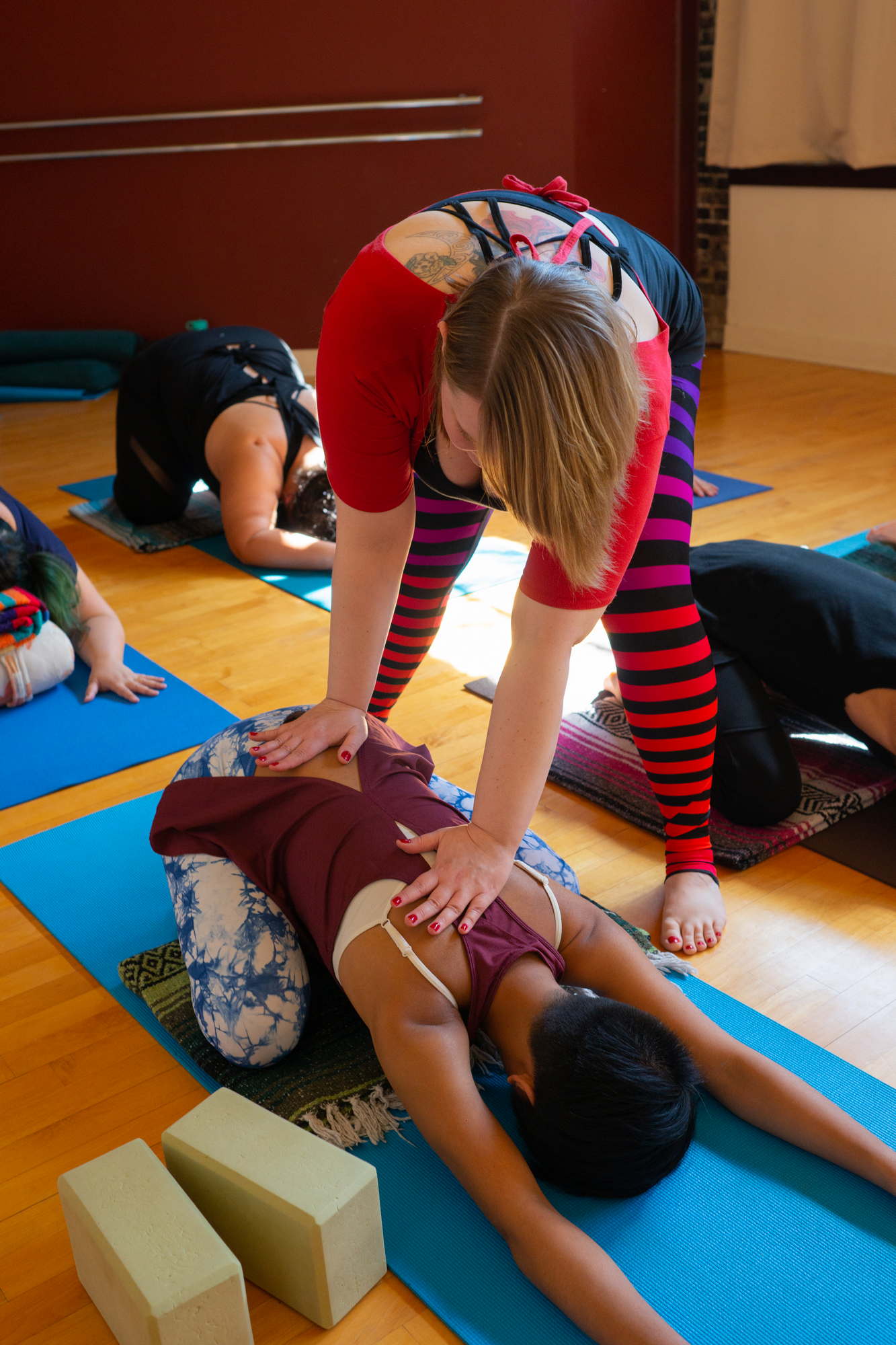  A fat yoga instructor assists a student with a pose on a mat