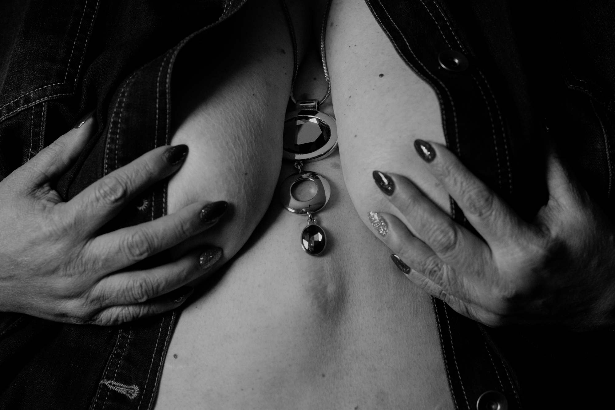  A woman covers her breasts with her hands, showing a necklace between them 