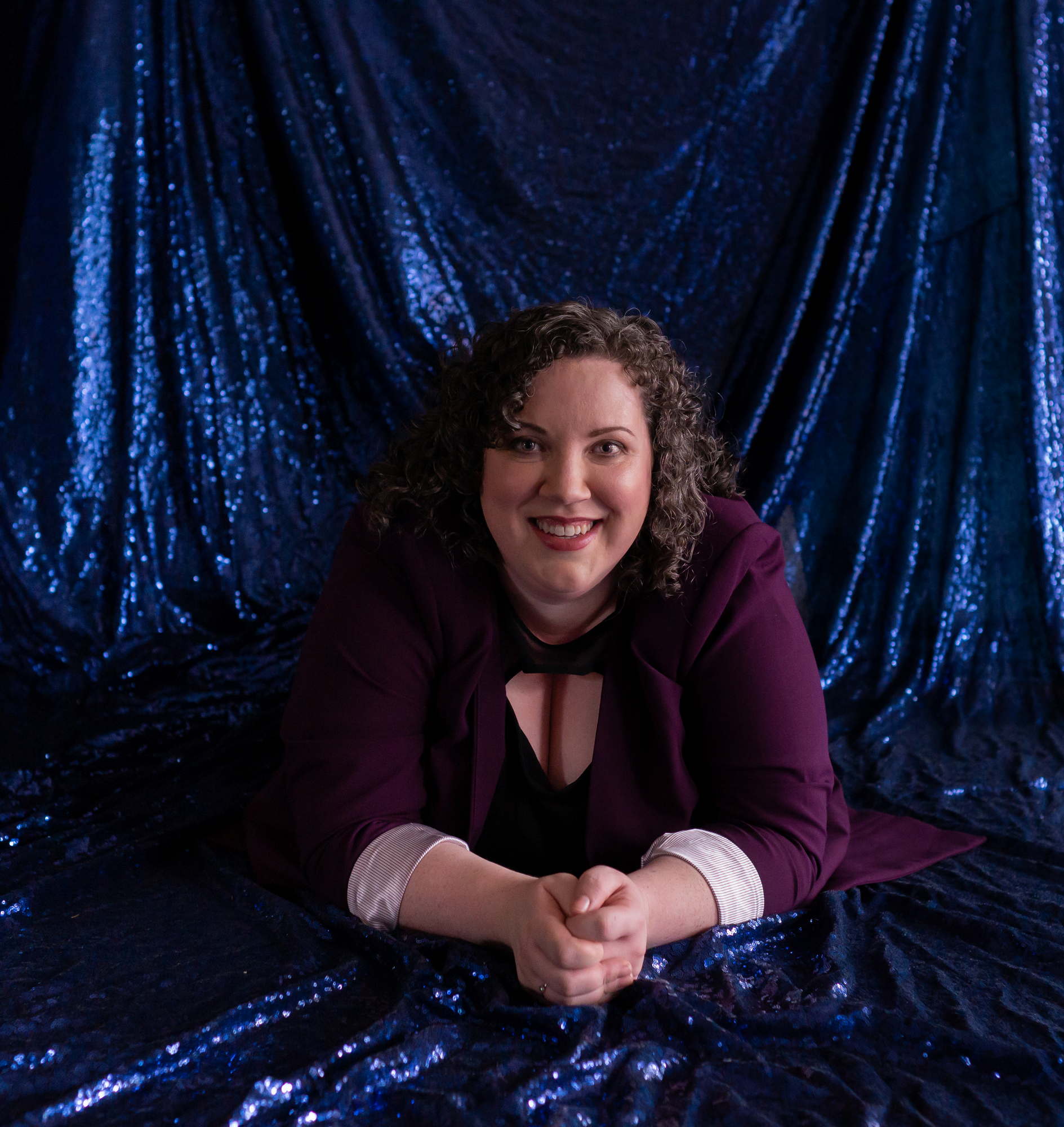 A fat woman in a purple blouse smiles confidently against a blue sequin background