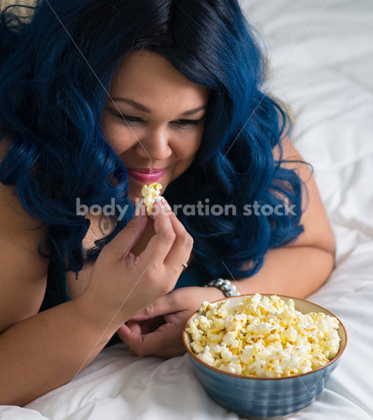 Royalty Free Stock Photo: Plus Size African American Woman Enjoys Popcorn and a Movie - Body Liberation Photos