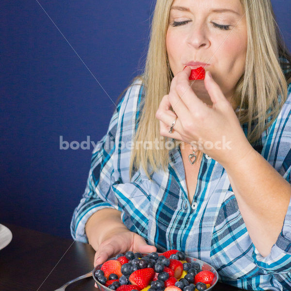 Royalty Free Stock Photo for Intuitive Eating: Plus Size Woman Eats Strawberry from Fruit Bowl - Body Liberation Photos