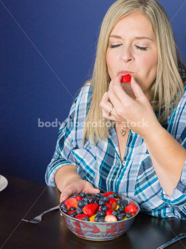 Royalty Free Stock Photo for Intuitive Eating: Plus Size Woman Eats Strawberry from Fruit Bowl - Body Liberation Photos