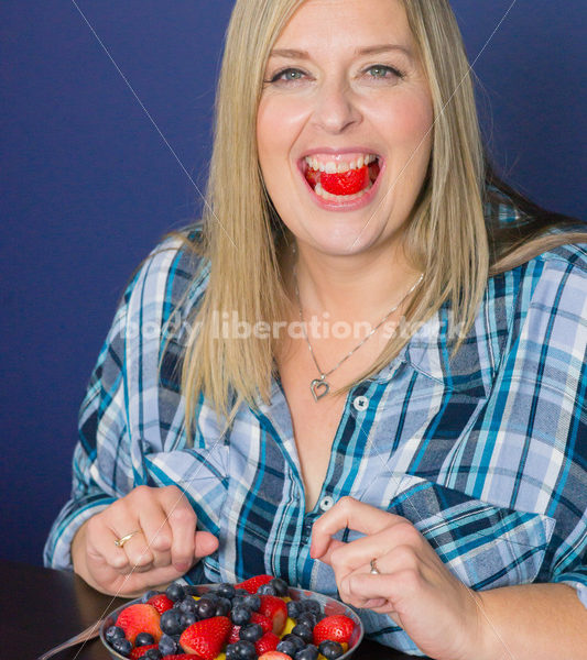 Royalty Free Stock Photo for Intuitive Eating: Plus Size Woman Eats Strawberry from Fruit Bowl - Body Liberation Photos