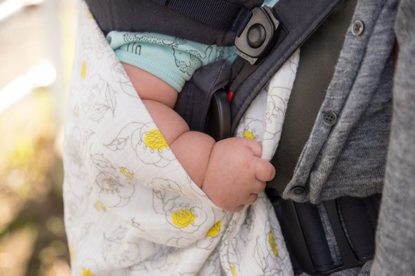 Image description: A fat white baby's arm is partially seen between an overlapping floral blanket, blue onesie sleeve and the body and strap of a car's seat and child safety seat. Image source: Al Soot on Unsplash