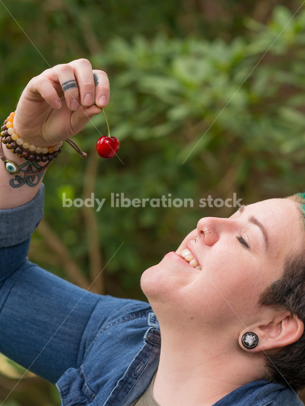 Diverse Gardening Stock Photo: Agender Person Eats Cherries in Garden - Body Liberation Photos
