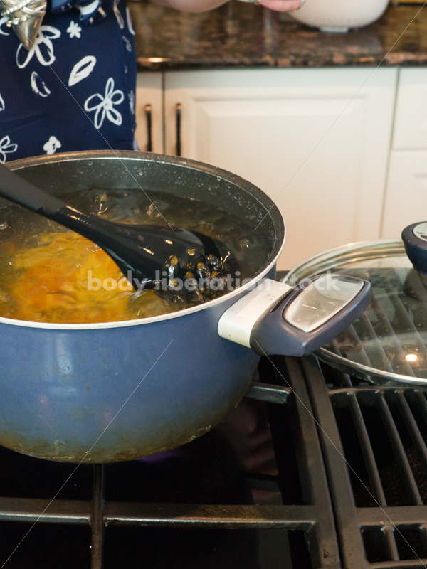 Eating Disorder Recovery Stock Photo: Woman Stirs Pasta in Pot of Water in Kitchen - Body Liberation Photos