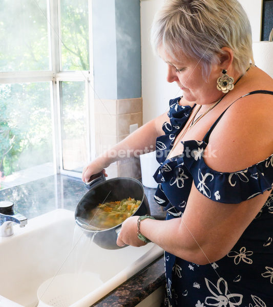 Eating Disorder Recovery Stock Photo: Woman Strains Pasta in Pot of Water in Kitchen - Body Liberation Photos