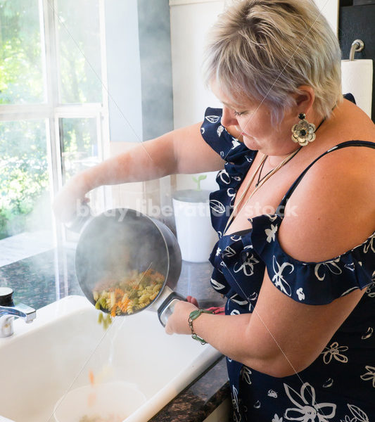 Eating Disorder Recovery Stock Photo: Woman Strains Pasta in Pot of Water in Kitchen - Body Liberation Photos