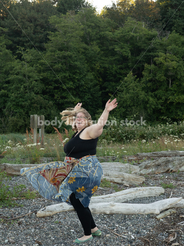 Joyful Movement Stock Image: Plus-Size Woman Twirls on Pebbled Beach at Dusk - Body Liberation Photos