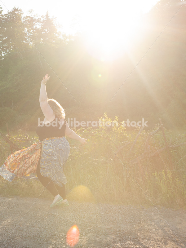Joyful Movement Stock Image: Plus-Size Woman Twirls on Rural Road at Golden Hour - Body Liberation Photos