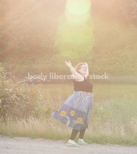 Joyful Movement Stock Image: Plus-Size Woman Twirls on Rural Road at Golden Hour - Body Liberation Photos