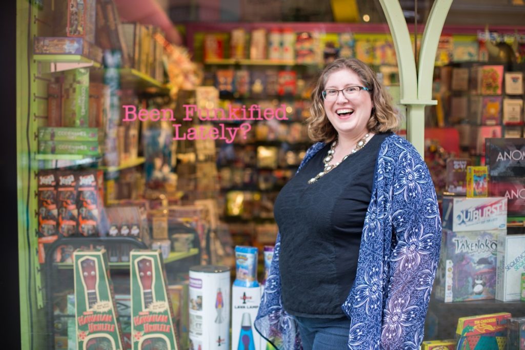 Lindley, a fat white woman, stands in front of a shop window that reads, Been Funkified?