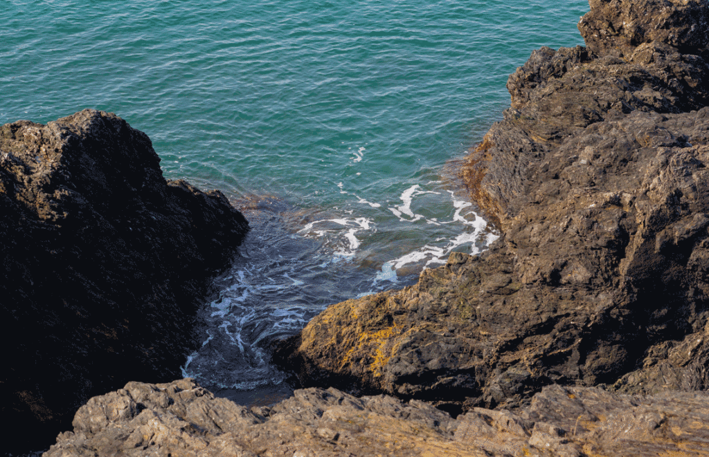 Blue water washes in small waves up onto brown sea rocks.