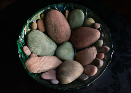 A green glass bowl of smooth pebbles in soft red and green tones and mixed sizes, stones Lindley found in a river in Idaho