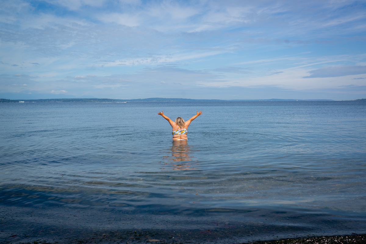 A size 32 plus-size woman raises her arms joyfully while standing in waist-deep water.