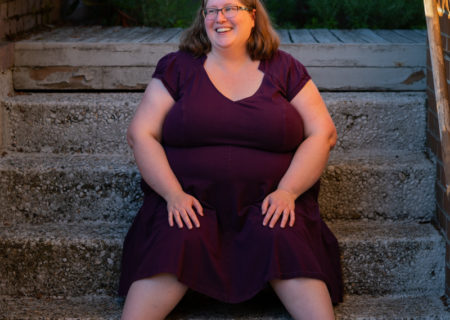 A fat white woman celebrating her 20th wedding anniversary sits on a set of gray steps, wearing glasses and a purple dress.