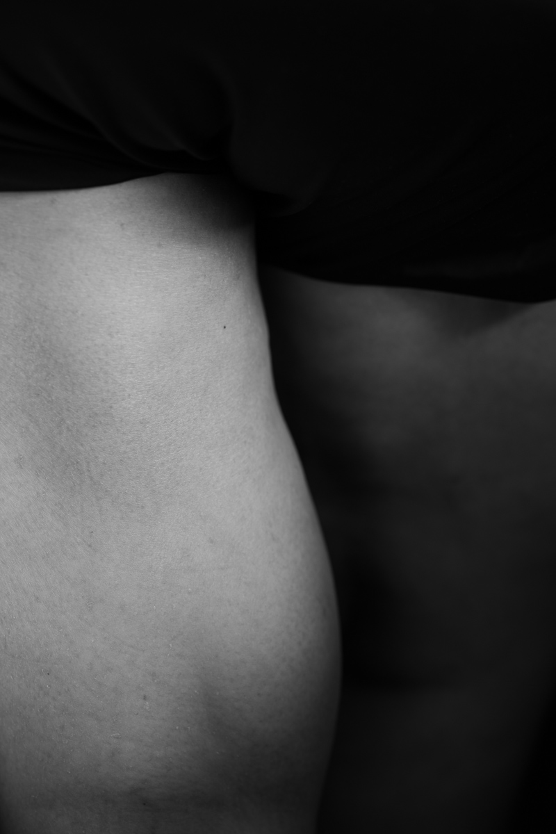 A black-and-white abstract photo of a fat person's thighs. One is in the light, while the other is in deep shadow.