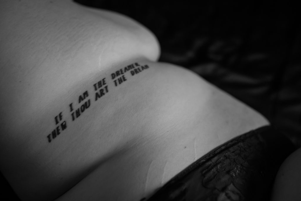 A fat woman's side with a tattoo in bold font that reads "If I am the dreamer, thou art the dream" in black and white during a boudoir photoshoot in the PNW
