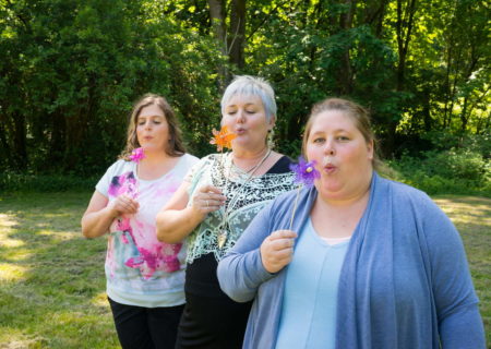 Three fat women stand in a sunny park and blow on pinwheels.