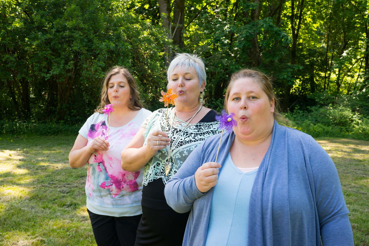 Three fat women stand in a sunny park and blow on pinwheels.
