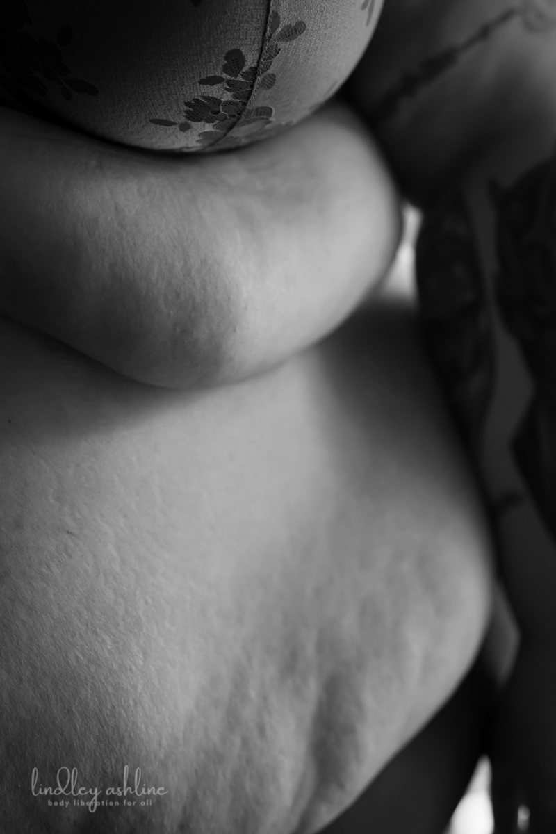 A close-up of a fat woman's side and belly rolls in black and white, with a bit of a bra and arm showing.
