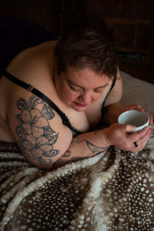 A fat woman holding a coffee cup looks downard during a photo session in the PNW