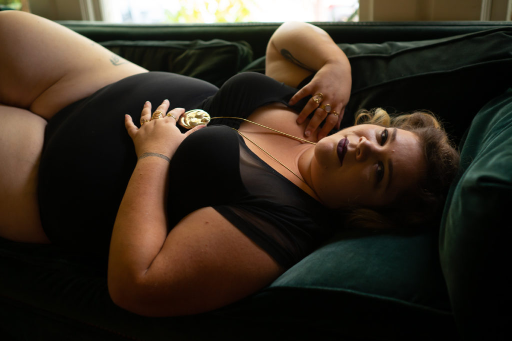 A fat woman holds a locket while reclining on a green velvet couch during a boudoir photo sessin in the PNW
