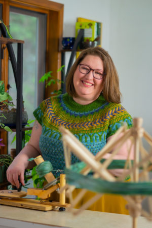 A fat woman in a colorful sweater smiles cheerfully at the camera during a business headshot session in the PNW