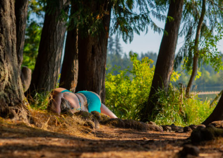 A fat woman in a blue bathing suit lies on the ground in a sun-dappled forest, cradled by tree roots.