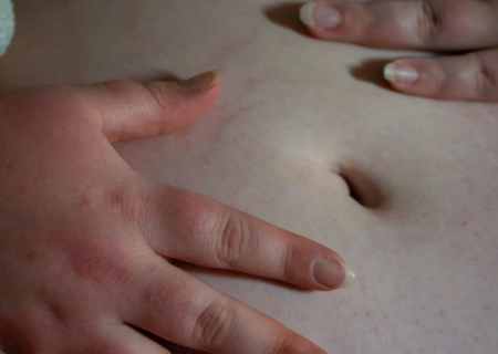 A fat woman's belly and hands in low light at a body liberation boudoir session in Seattle.
