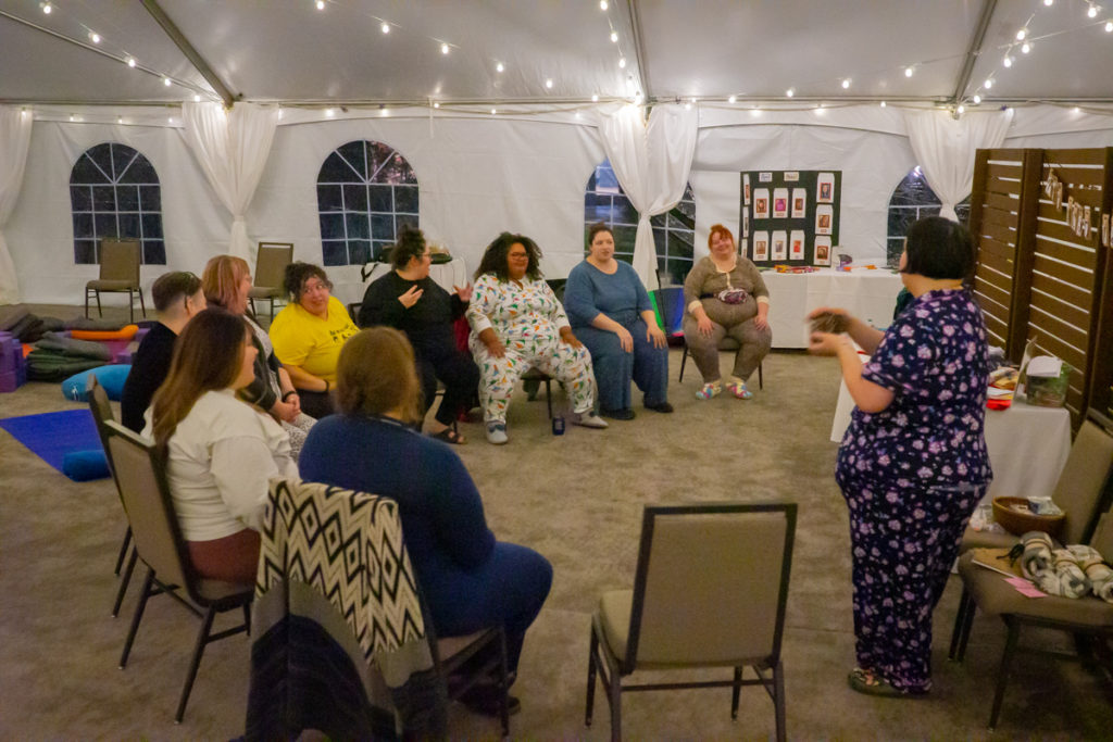   A group of fat people gather around and listen to a fat speaker in a tent 