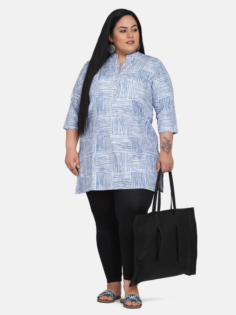 Image description: A fat person wearing a tunic-style top with blue cross hatched squares printed on it looks off to one side