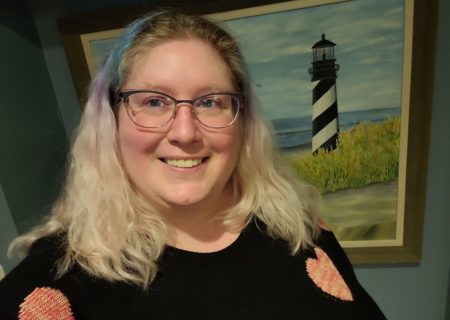 Lindley, a fat white woman, in glasses and standing in front of a painting of a lighthouse